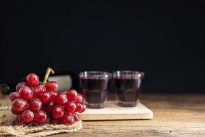 A bunch of red grapes with red grape juice in a glass placed on a wooden table or red wine, delicious natural healthy juice drink. photo