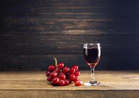 rojo uva jugo en un vaso metido en un de madera mesa o rojo vino, un delicioso natural sano jugo beber. con un manojo de Fresco rojo uvas desde el jardín foto