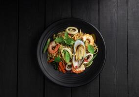 Seafood drunken spaghetti with shrimp squid clams chili, and basil. Thai food. Healthy Asian in a plate on a black background table. Top view. photo