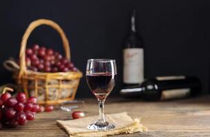 rojo uva jugo en un vaso metido en un de madera mesa o rojo vino, un delicioso natural sano jugo beber. con un manojo de Fresco rojo uvas desde el jardín foto