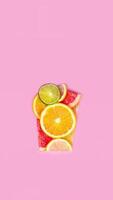 creativo plano laico jugo concepto. rebanado agrios naranja, Lima, pomelo, limón, frutas hacer jugo vaso forma rosado antecedentes vertical vídeo stopmotion animación foto