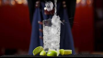 Close up of a professional bartender is mixing an alcoholic cocktail with professional crystal long lasting ice cubes to customers at the bar or disco club. Professional bartender masterly creating video