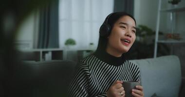 Portrait of Happy young asian woman enjoy listening to the music with wireless headphones while sitting drink coffee on sofa in living room at home, Leisure and lifestyle,Free time photo