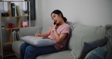 Portrait of Young woman talking mobile phone and take notes in a notebook while sitting on sofa at home office. photo