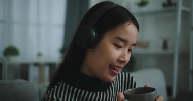 Portrait of Happy young asian woman enjoy listening to the music with wireless headphones while sitting drink coffee on sofa in living room at home, Leisure and lifestyle,Free time photo