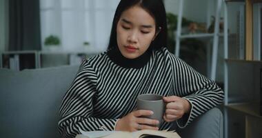 retrato de contento joven asiático mujer Bebiendo Mañana café o té y leyendo en vivo habitación a hogar en fin de semana. ocio y estilo de vida, gratis hora foto