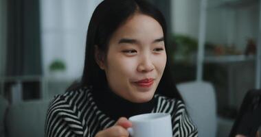 Portrait of Happy young asian woman sit on sofa enjoy chatting on mobile phone while drinking coffee in morning in living room,Free time,take break,smiling photo