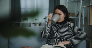 retrato de contento joven asiático mujer Bebiendo Mañana café o té y leyendo en vivo habitación a hogar en fin de semana. ocio y estilo de vida, gratis hora foto