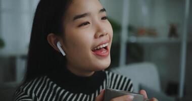 retrato de contento joven asiático mujer disfrutar escuchando a el música con inalámbrico auriculares mientras sentado bebida café en sofá en vivo habitación a hogar, ocio y estilo de vida, gratis hora foto