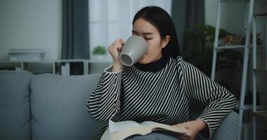 retrato de contento joven asiático mujer Bebiendo Mañana café o té y leyendo en vivo habitación a hogar en fin de semana. ocio y estilo de vida, gratis hora foto