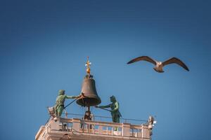 Seagull flying over iconic bell tower in Venice, Italy against clear blue sky photo