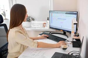 Portrait of a remote worker. An adult woman sits at a table in front of a computer and draws up a costly estimate. Confident young lady freelancer working from home. photo