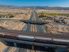 Aerial View of Desert Highway Interchange with Train Tracks and Rugged Mountains Under Clear Blue Sky photo