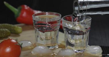 Pour vodka from a bottle into shot glasses with ice cubes on the table photo