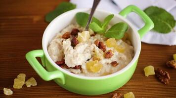 cooked boiled sweet oatmeal with nuts and candied fruits in a bowl on a wooden table video