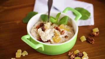 cooked boiled sweet oatmeal with nuts and candied fruits in a bowl on a wooden table video