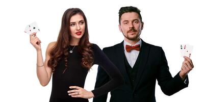 Woman in black dress and man in classic suite are showing two aces. They posing isolated on white studio background. Gambling, poker, casino. Close-up photo