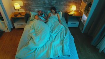 Top view of young couple having a conversation late at night in bed under the sheet with blue moon light in the room. video