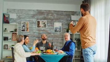 espalda ver de joven hombre utilizando teléfono inteligente a tomar un grupo foto de su familia a cena. video