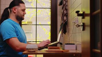 Freelancer working on laptop in his kitchen while a small essential oil diffuser is steaming next to him video