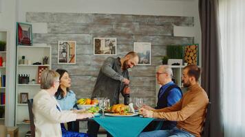 Bearded man at head of the table opening a bottle of red wine at family lunch. Dinner with friends and family video