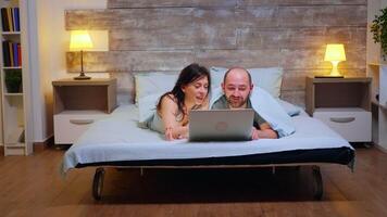 Zoom in shot of couple wearing pajamas lying in bed using laptop. video