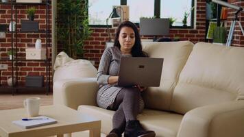 telelavoratore dire bugie su divano, remoto l'esecuzione compiti nel personale ufficio. rilassato libero professionista immissione dati su il computer portatile mentre Lavorando a partire dal casa, telecamera un' dolly nel vicino su tiro video