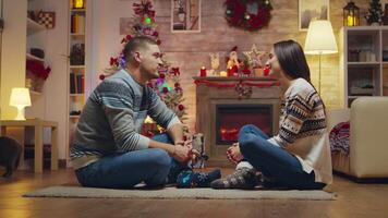 hermosa joven Pareja mirando a cada otro sentado en el alfombra celebrando Navidad en frente de chimenea. video