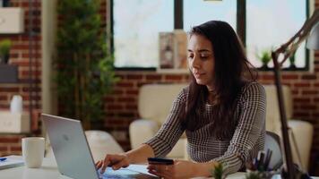 Happy woman stoked on doing online shopping, carefully typing credit card information on laptop. Indian person adding payment method on website while in cozy stylish warm home, camera B panning shot video