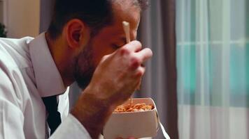 Close up of businessman with tie eating noodles from a box using chopsticks. video