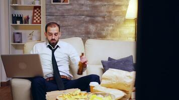 Businessman reaching out for his beer while working on laptop from home. Entrepreneur in suit. video