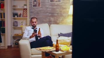 Tired businessman after long day of work browsing on phone and drinking beer. Junk food. video