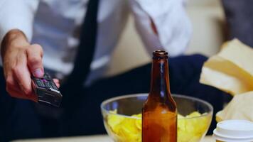 Close up of businessman sitting on couch using remote control. Beer on table. video