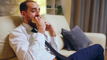 affärsman i formell ha på sig Sammanträde på soffa äter en burger och talande på de telefoner efter en tröttsam dag. video