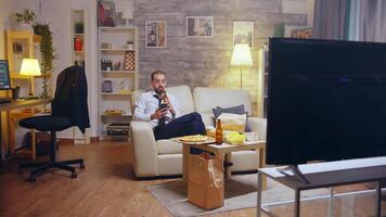 Young businessman in suit and tie relaxing drinking beer and browsing on phone after a hard day at work, video