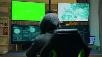 Back view of hacker wearing a hoodie using computer with green screen. video