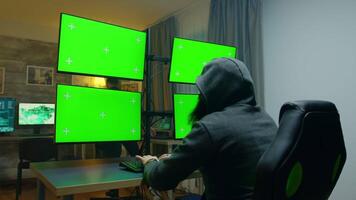 Bearded hacker hiding his face wearing a hoodie using computer with green screens. video