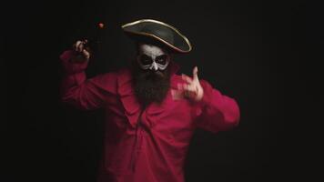 Man with beard dressed up like a drunk pirate using his pistol for halloween over black background. video