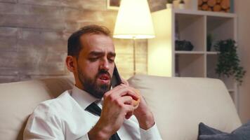 Young entrepreneur in formalwear eating a burger while having a business conversation on the phone. video