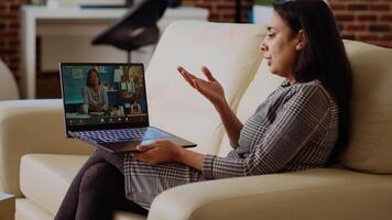 Indian remote professional holding q and a session with multiethnic webinar participants via teleconference meeting. Internet videocall host on couch at home engaging in discussions with trainees video