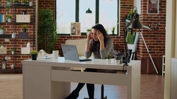 stressato oberati di lavoro indiano dipendente lottando per concentrato mentre Lavorando a partire dal casa, ferire a partire dal male alla testa. stanco telelavoratore sensazione nausea mentre Lavorando su computer portatile, telecamera un' video