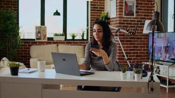 glimlachen vrouw opgewonden Aan aan het doen online winkelen, voorzichtig typen debiteren kaart informatie Aan laptop toetsenbord. persoon toevoegen betaling methode Aan website terwijl in modern appartement leven kamer, camera een video