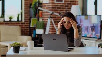 estressado sobrecarregado indiano empregado lutando para concentrado enquanto trabalhando a partir de lar, machucando a partir de dor de cabeça. cansado teletrabalhador sentindo-me náusea enquanto trabalhando em computador portátil, Câmera b video