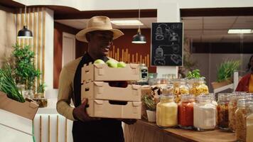 Local vendor placing crates with freshly harvested fruits on grocery store display, recommending organic produce to regular customer. African american farmer restocking all merchandise. Camera B. video