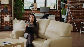 Smiling person excited to catch up with friends during online meeting session while relaxing in modern stylish apartment living room. Woman chatting with mates in videocall using laptop, camera A video