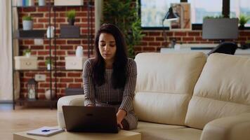 indisch Telearbeiter Sitzung auf Couch, konzentriert auf Fertigstellung Aufgaben im persönlich Büro. Fernbedienung Arbeiter Konzentration auf korrekt Eingabe Daten auf Laptop, eilen zu Komplett Projekt Vor Frist video