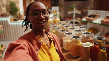 POV of african american client promoting local bio supermarket on social media networks, filming video online to create ad. Woman presenting additives free bulk items and produce. Handheld shot.