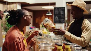 African american farmer recommends products for regular buyer, presenting all organic ingredients for a family recipe. Merchant showing chemicals free sauce and homemade pasta. Camera B. video