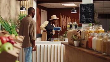 Vegan customer using card at pos to pay for natural food alternatives, purchasing homemade sauces and pantry supplies. African american man shopping for organic additives free products at local market. Camera B. video