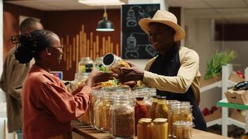 Local seller recommending fresh bio produce to regular client, showing new organic additives free products. Merchant presenting natural eco friendly bulk items in recyclable jars. Camera A. video